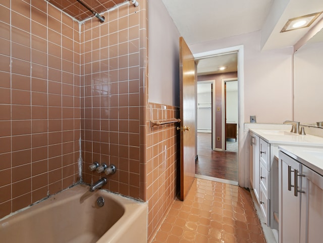 bathroom with tile walls, tile patterned flooring, tiled shower / bath combo, and vanity