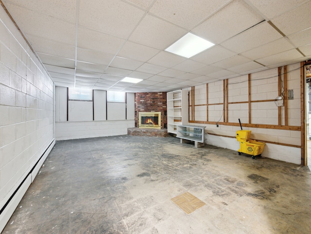 basement with a drop ceiling, a brick fireplace, and baseboard heating