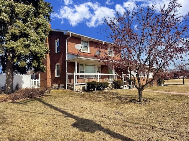 view of front of home featuring brick siding, a porch, a front yard, and fence