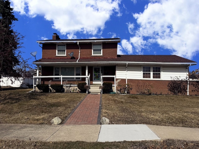 traditional-style home featuring a porch, a front lawn, brick siding, and a chimney