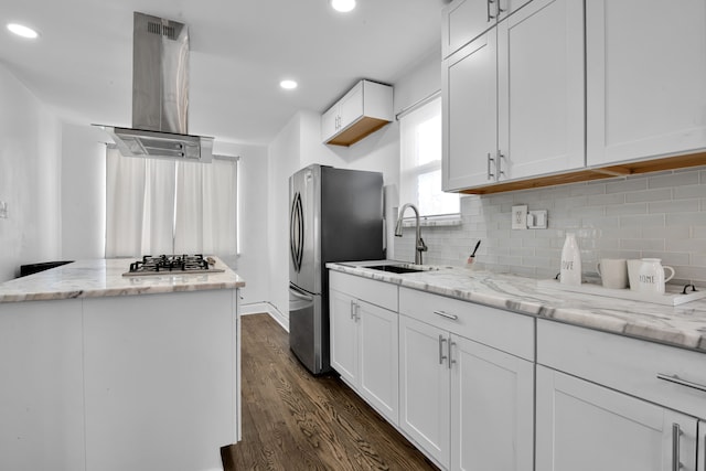 kitchen with light stone counters, white cabinetry, island exhaust hood, and a sink