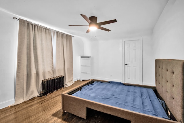 bedroom with radiator heating unit, baseboards, ceiling fan, and wood finished floors