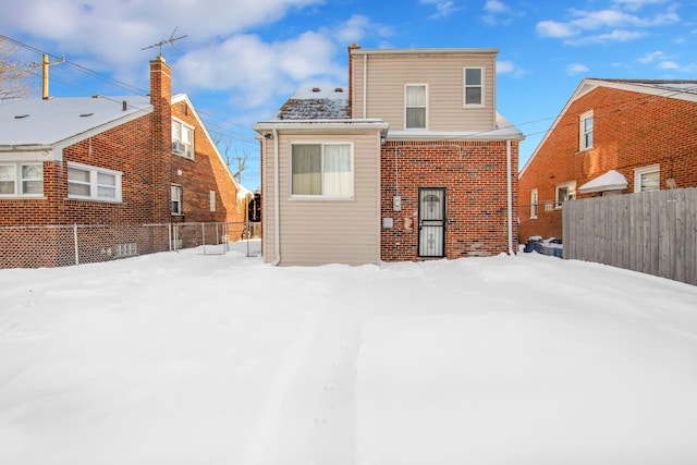 snow covered rear of property with brick siding and fence