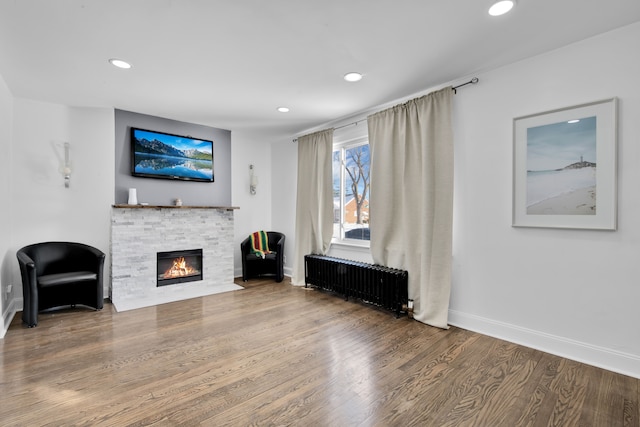 living area with wood finished floors, radiator heating unit, baseboards, a glass covered fireplace, and recessed lighting