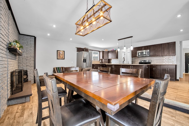 dining room with light wood-type flooring, a brick fireplace, brick wall, and recessed lighting