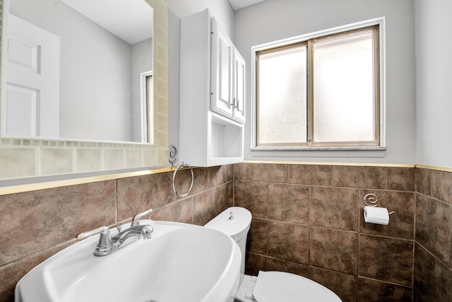 half bath with toilet, a wainscoted wall, tile walls, and a sink