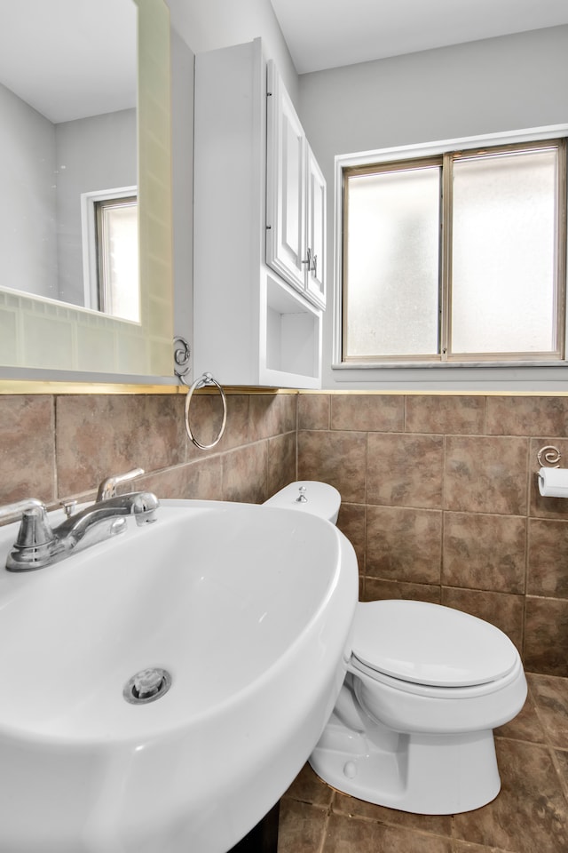 half bath with toilet, tile walls, and a sink