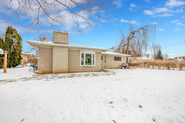 snow covered back of property featuring a chimney and brick siding