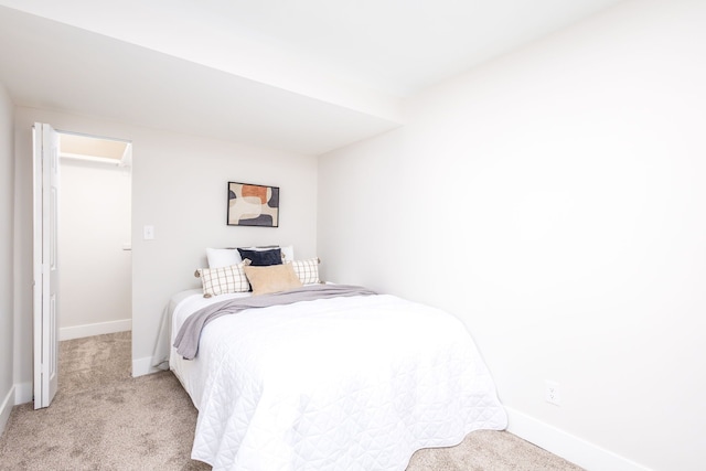 bedroom with light carpet, a walk in closet, and baseboards