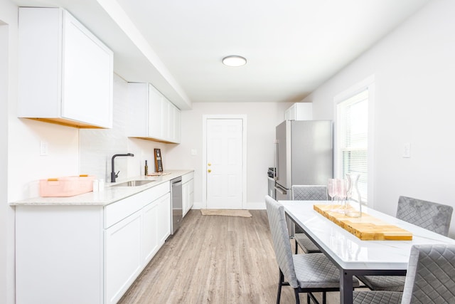 kitchen featuring stainless steel appliances, light wood-style floors, white cabinetry, a sink, and baseboards