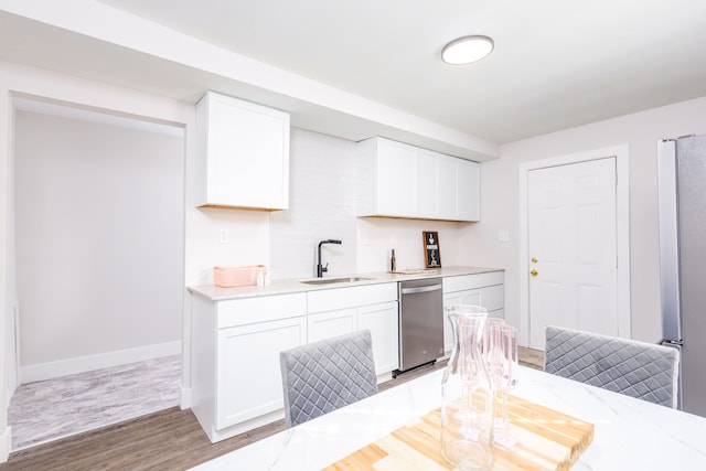 kitchen with baseboards, white cabinets, wood finished floors, stainless steel dishwasher, and a sink