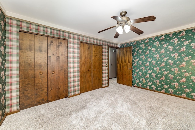 unfurnished bedroom featuring carpet floors, two closets, ceiling fan, and wallpapered walls