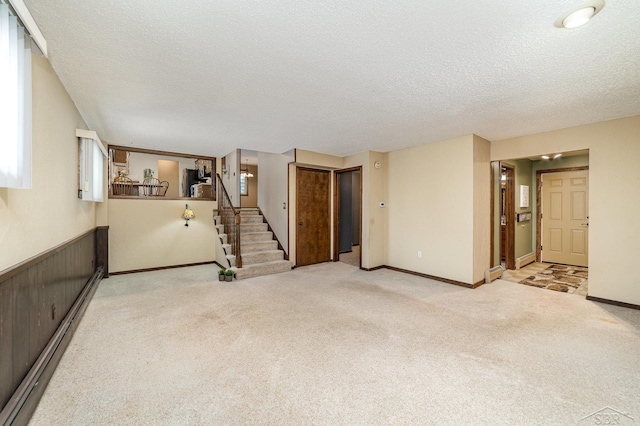 carpeted empty room with stairs, baseboards, wainscoting, and a textured ceiling