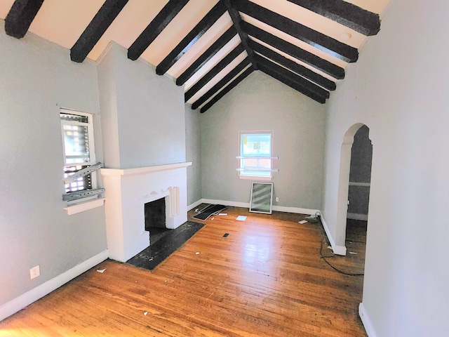 unfurnished living room featuring a fireplace with flush hearth, wood finished floors, beam ceiling, and baseboards