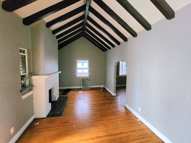 unfurnished living room with arched walkways, a fireplace, wood finished floors, beamed ceiling, and baseboards