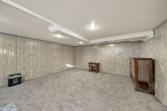 basement featuring carpet floors, a textured ceiling, and wood walls