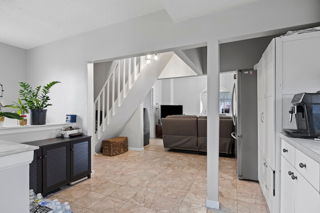 kitchen with marble finish floor, light countertops, freestanding refrigerator, white cabinets, and a textured ceiling