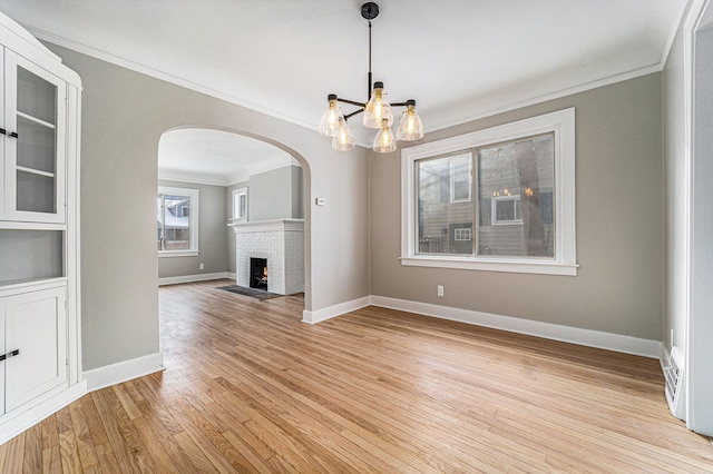 unfurnished living room featuring ornamental molding, light hardwood / wood-style flooring, a brick fireplace, and a notable chandelier