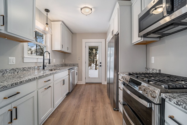 kitchen with white cabinetry, hanging light fixtures, stainless steel appliances, light stone countertops, and sink