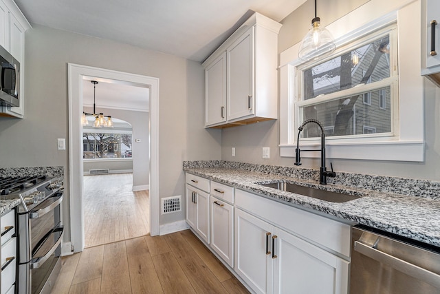 kitchen with white cabinetry, light wood-type flooring, sink, light stone counters, and appliances with stainless steel finishes