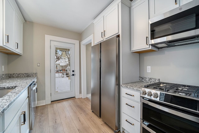 kitchen featuring white cabinetry, stainless steel appliances, light stone counters, and light hardwood / wood-style flooring