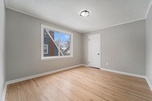 empty room with a textured ceiling, crown molding, and light hardwood / wood-style floors