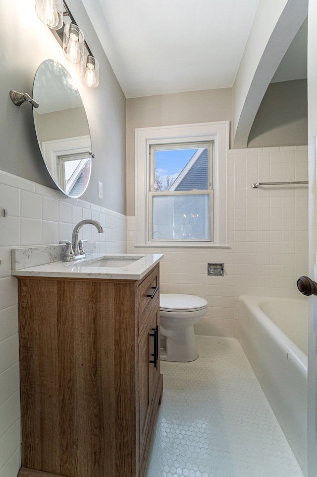 bathroom featuring tile patterned floors, toilet, tile walls, and a bath