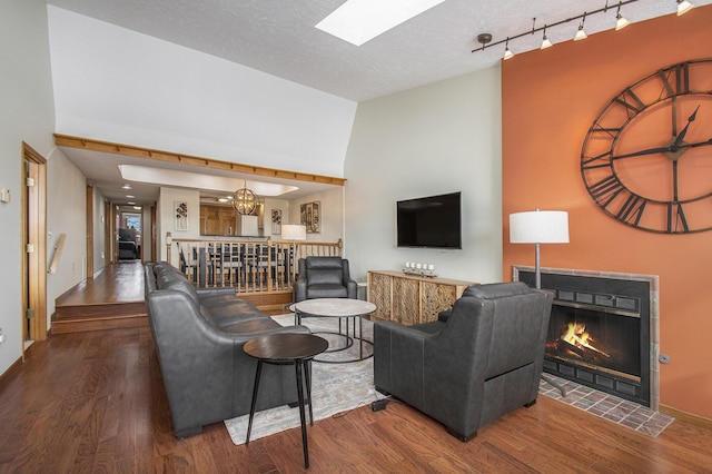 living room with dark wood-type flooring, a textured ceiling, a skylight, and a tiled fireplace