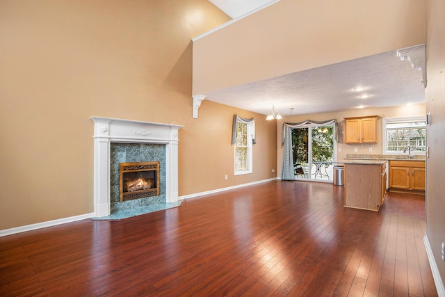 unfurnished living room featuring dark hardwood / wood-style flooring, a high end fireplace, a notable chandelier, sink, and a high ceiling