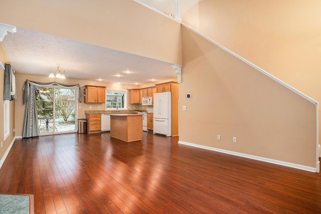 kitchen with a notable chandelier, dark wood-type flooring, white appliances, a center island, and sink