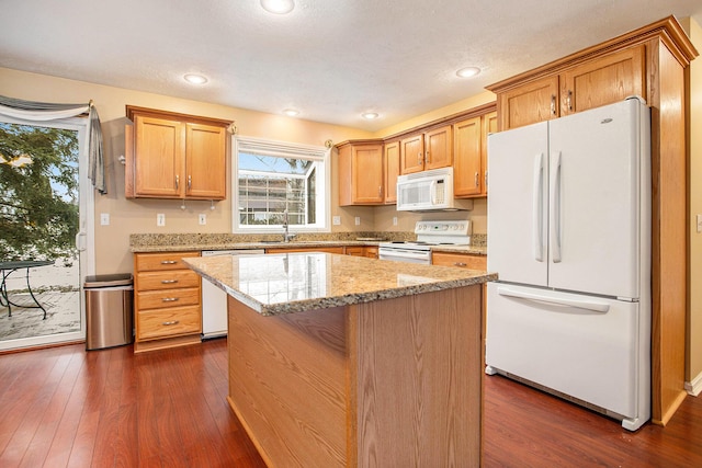 kitchen featuring dark wood-type flooring, white appliances, a kitchen island, and light stone counters