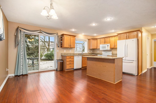 kitchen featuring white appliances, dark wood-type flooring, light stone countertops, pendant lighting, and a center island