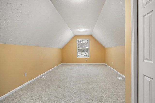 additional living space with a textured ceiling, light carpet, and lofted ceiling