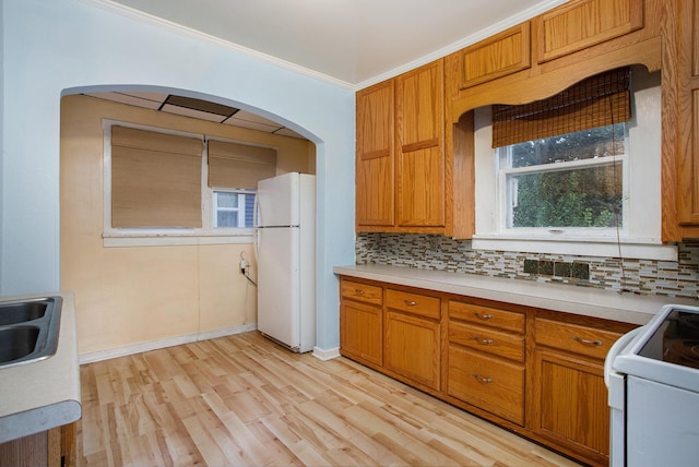 kitchen with light wood-type flooring, a wealth of natural light, white appliances, crown molding, and decorative backsplash