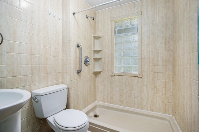 bathroom with tiled shower, sink, tile walls, and toilet