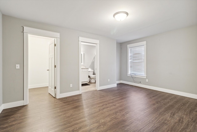 unfurnished bedroom featuring connected bathroom, dark hardwood / wood-style floors, and a walk in closet