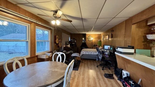 dining area featuring light wood-type flooring, a paneled ceiling, wood walls, and ceiling fan