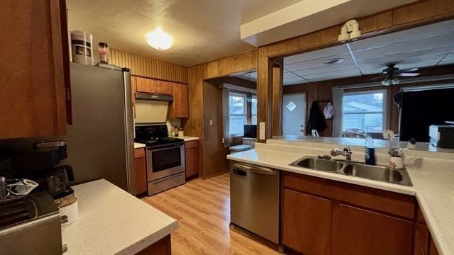 kitchen featuring appliances with stainless steel finishes, sink, light hardwood / wood-style flooring, ceiling fan, and wooden walls