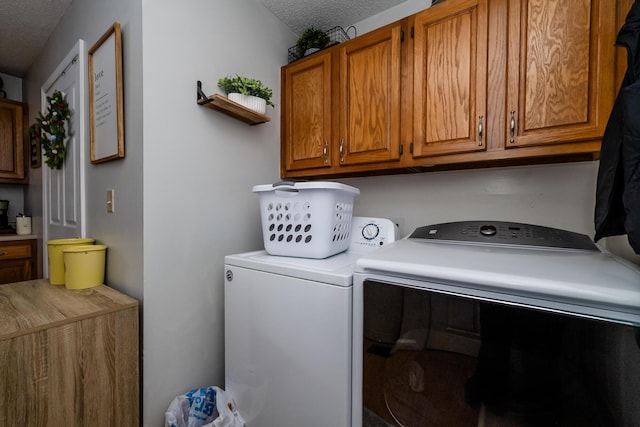 clothes washing area with a textured ceiling, cabinets, and washing machine and clothes dryer