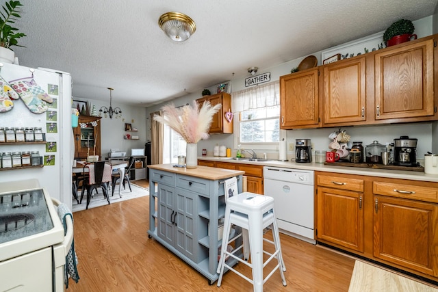 kitchen featuring sink, white appliances, a textured ceiling, and light wood-type flooring