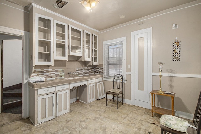 kitchen featuring tasteful backsplash, white cabinetry, crown molding, and tile counters