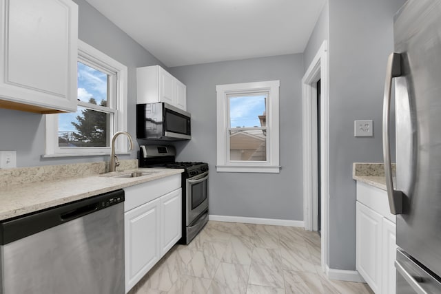 kitchen with marble finish floor, stainless steel appliances, a wealth of natural light, white cabinetry, and a sink