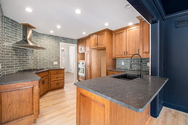 kitchen featuring sink, appliances with stainless steel finishes, wall chimney range hood, and light hardwood / wood-style floors