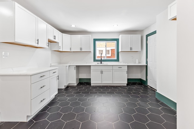 kitchen with white cabinetry, sink, dark tile patterned flooring, and light stone counters