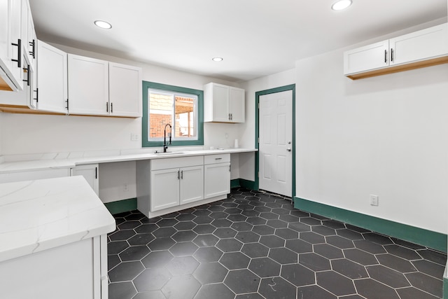 kitchen with white cabinetry, sink, and light stone counters