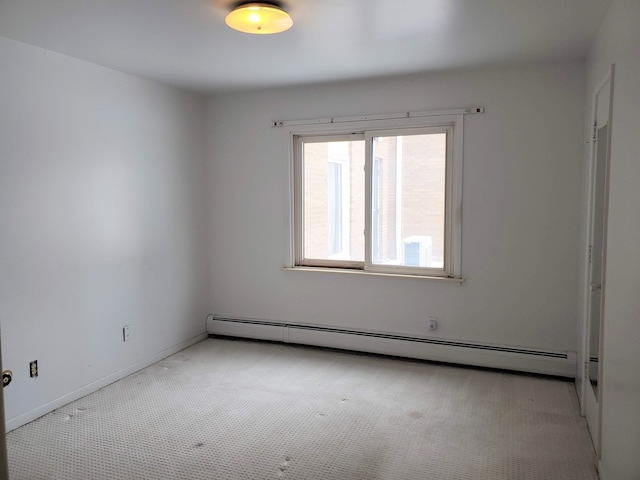 carpeted empty room featuring a baseboard heating unit