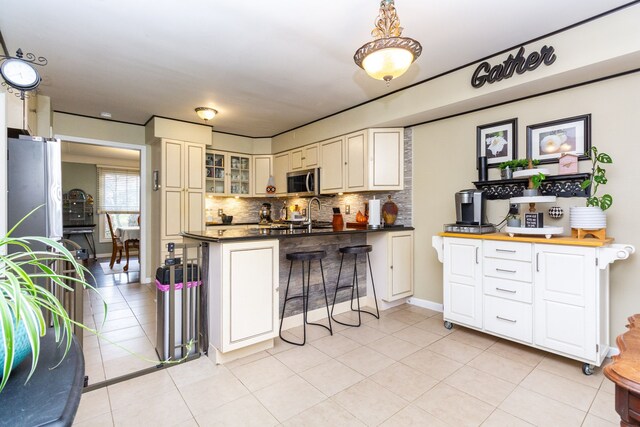 kitchen with appliances with stainless steel finishes, light tile patterned flooring, backsplash, sink, and kitchen peninsula