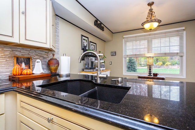 kitchen featuring sink, backsplash, dark stone counters, and hanging light fixtures