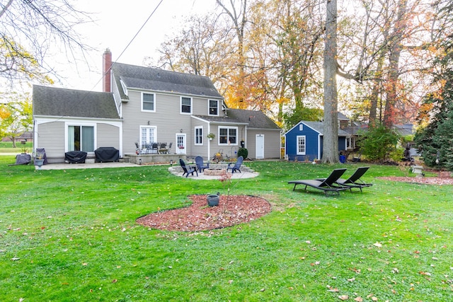 rear view of house with an outdoor structure, a fire pit, a lawn, and a patio area