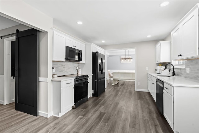 kitchen featuring white cabinetry, a barn door, black appliances, sink, and dark hardwood / wood-style floors